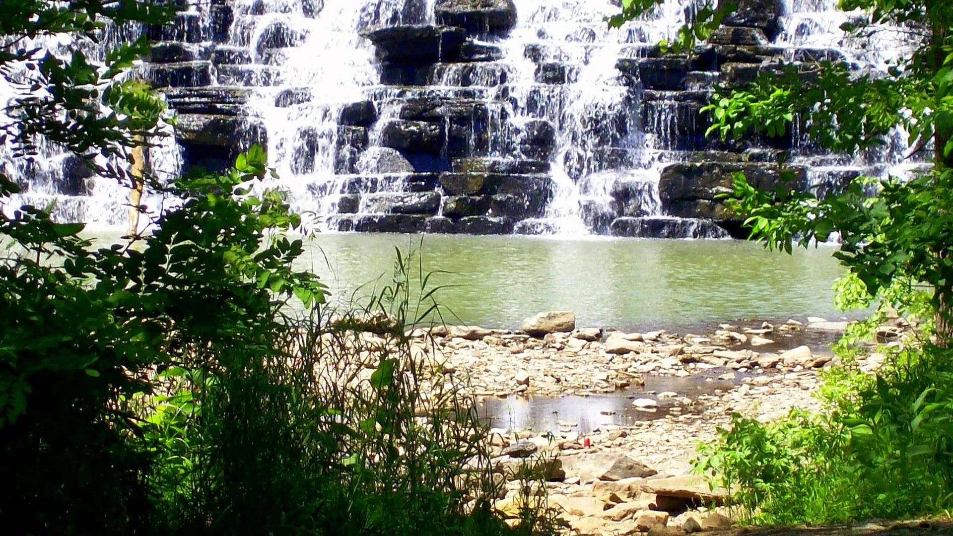 Breiter Kaskadenwasserfall zwischen Felsen und Wald im Devil’s Den State Park