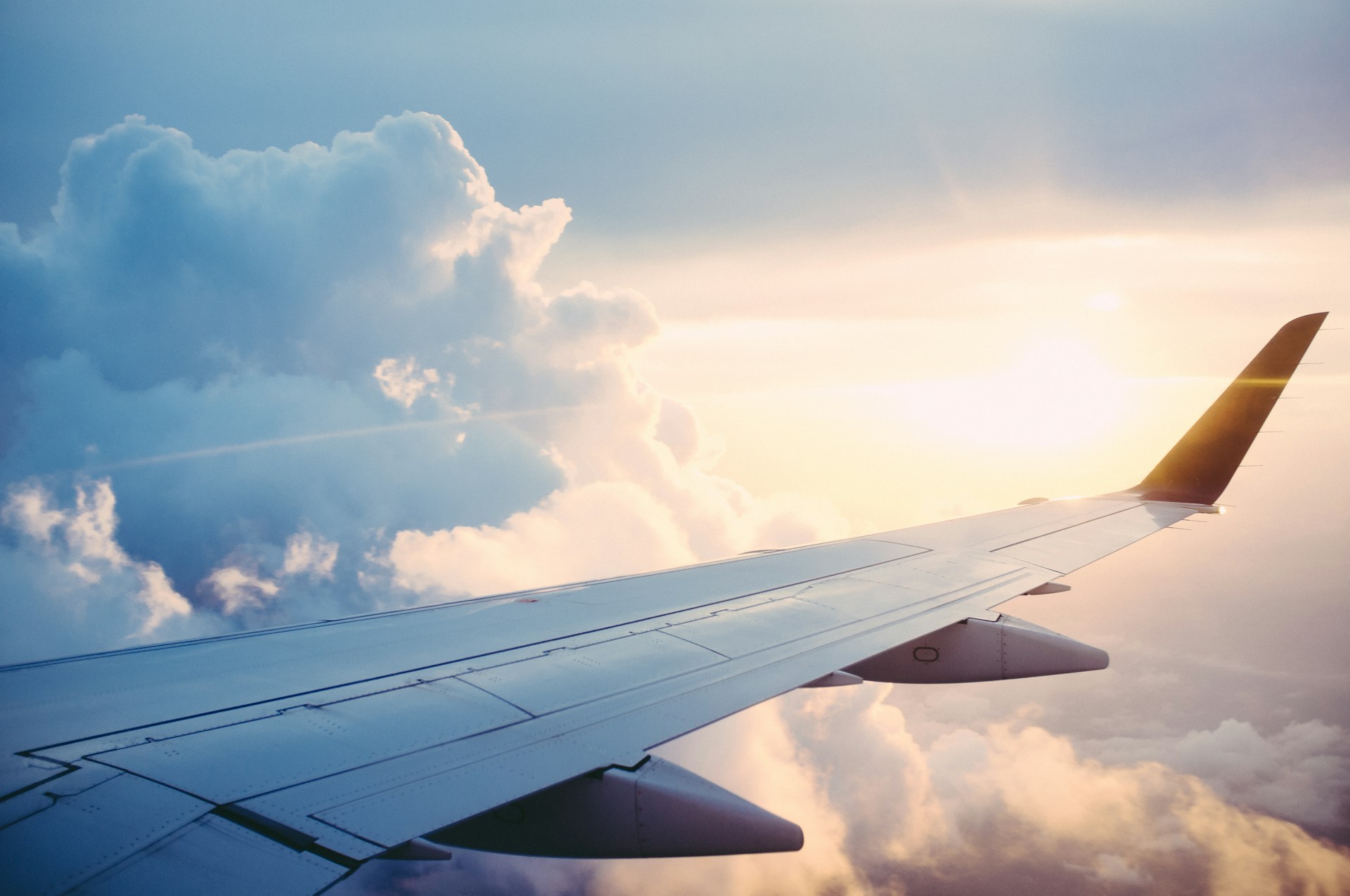 Blick aus dem Flugzeugfenster auf Wolken, Tragfläche und warmes Sonnenlicht