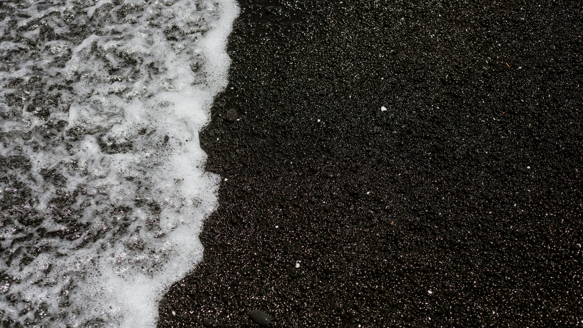 Weiße Brandung läuft über den schwarzen Lavastrand an der Kīholo Bay