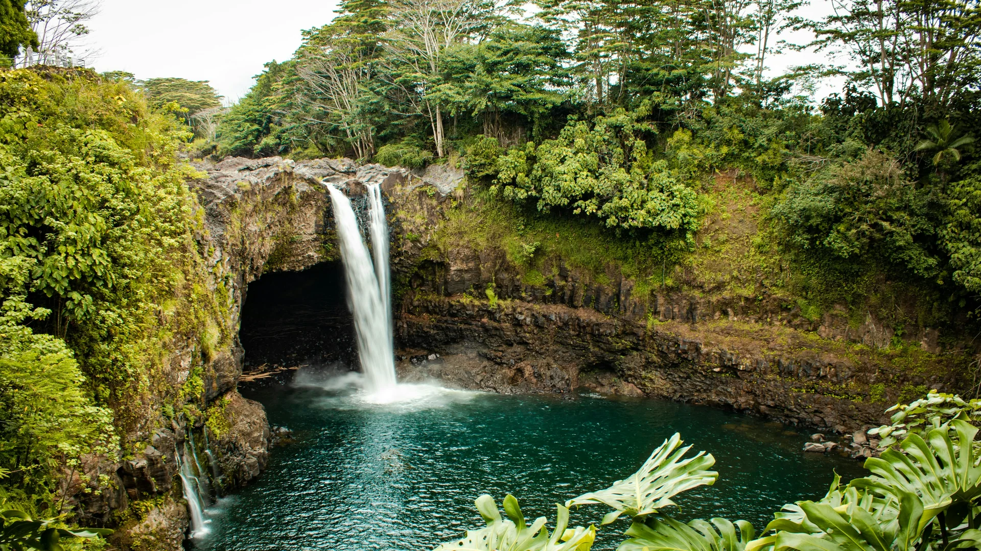 Rainbow Falls stürzt zwischen dichtem tropischem Grün in ein dunkles Becken