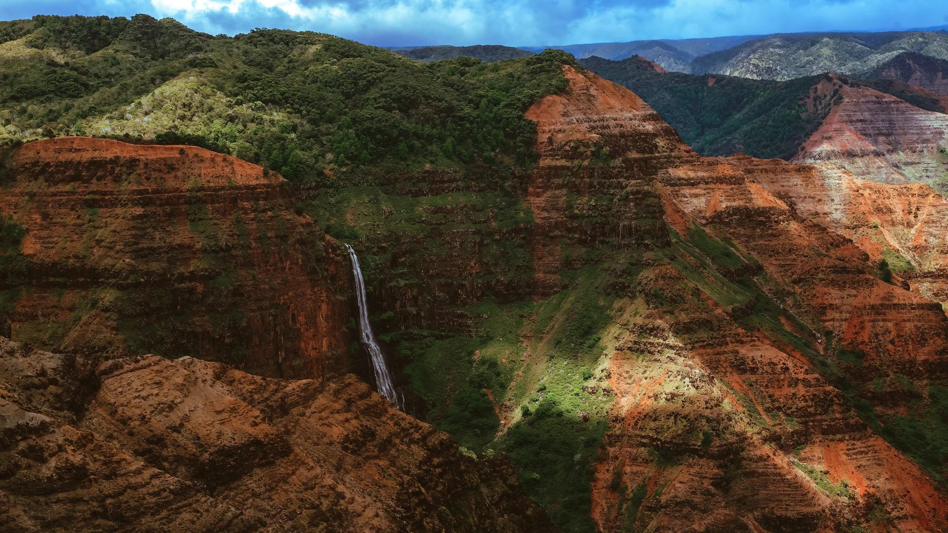 Ein schmaler Wasserfall fällt durch die roten Felswände des Waimea Canyon