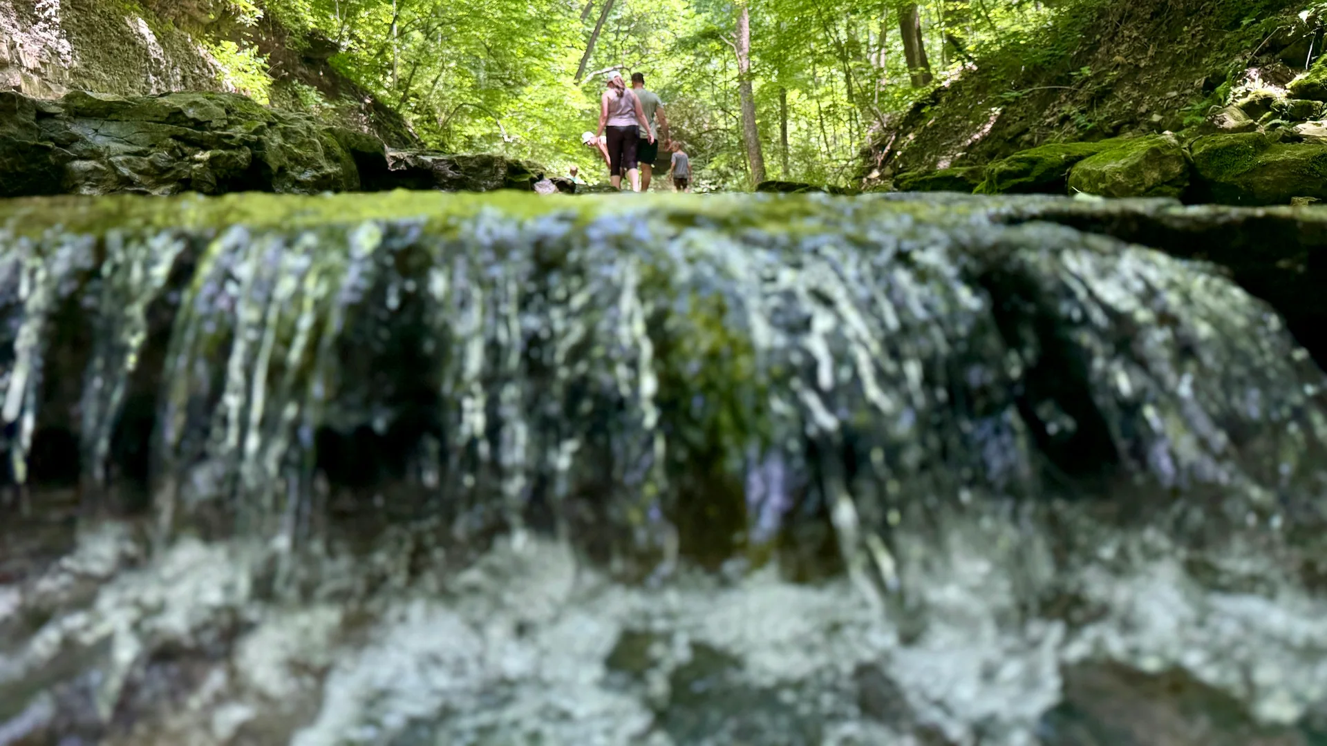 Wanderer stehen an einem kleinen Wasserfall im bewaldeten Clifty Falls State Park