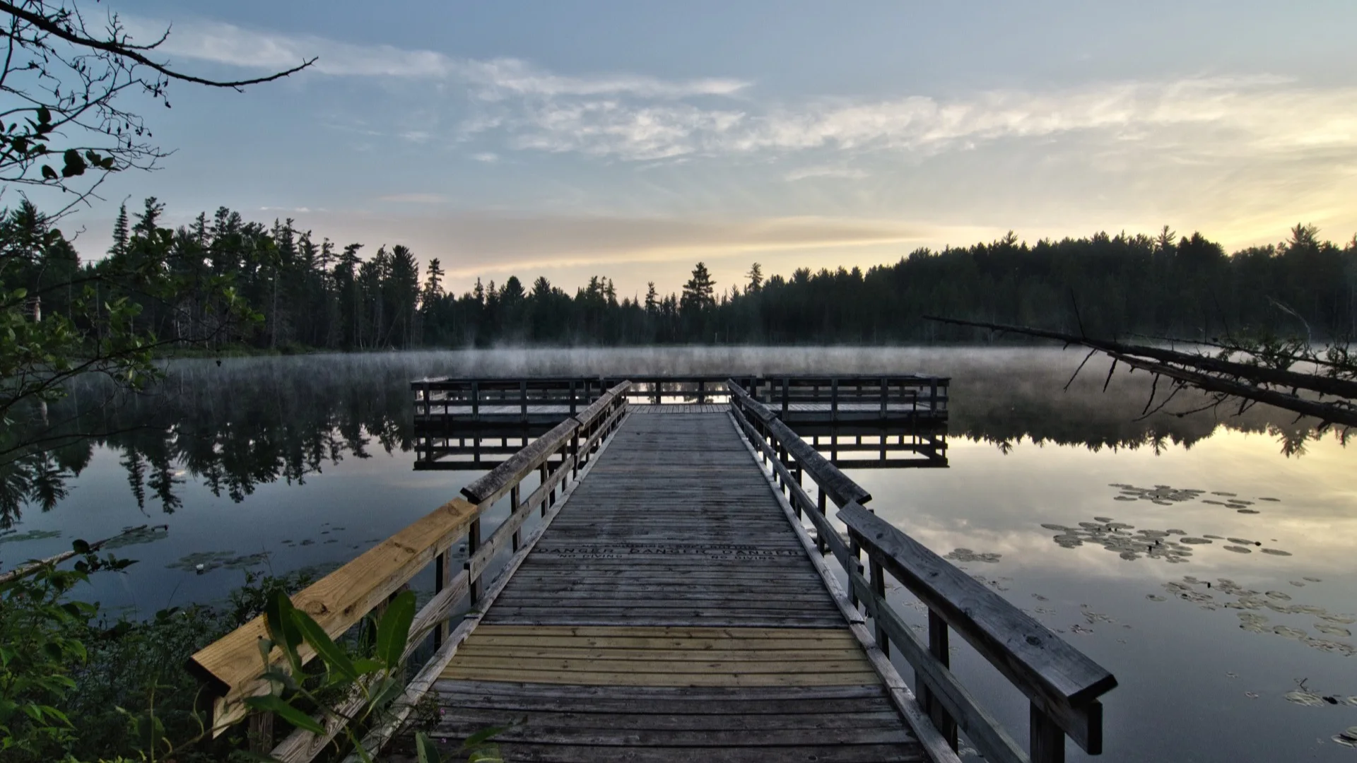 Steg über dem ruhigen Bright Lake im Hartwick Pines State Park am frühen Morgen