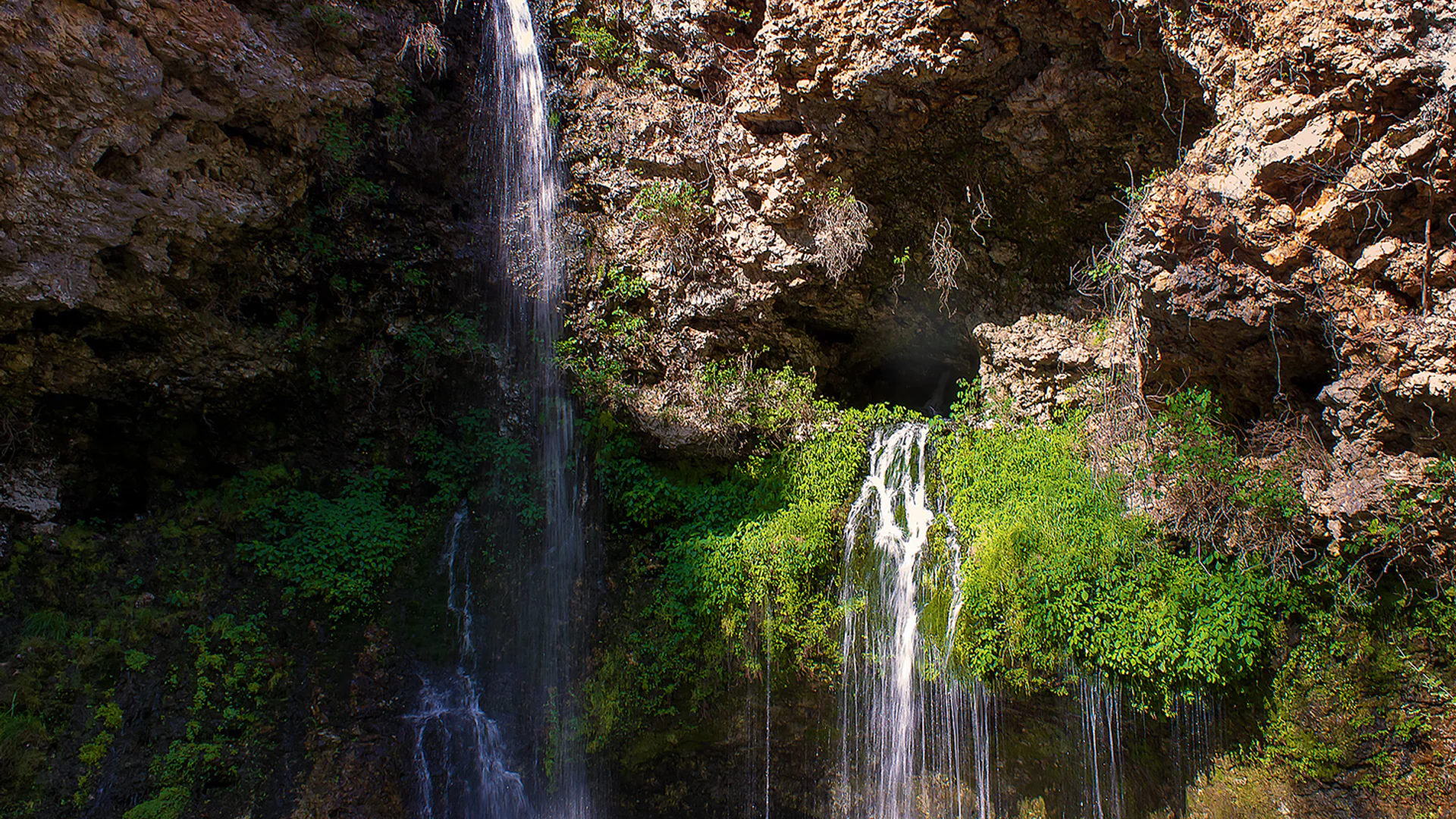Natural Falls fällt durch eine grüne, felsige Schlucht in ein ruhiges Becken