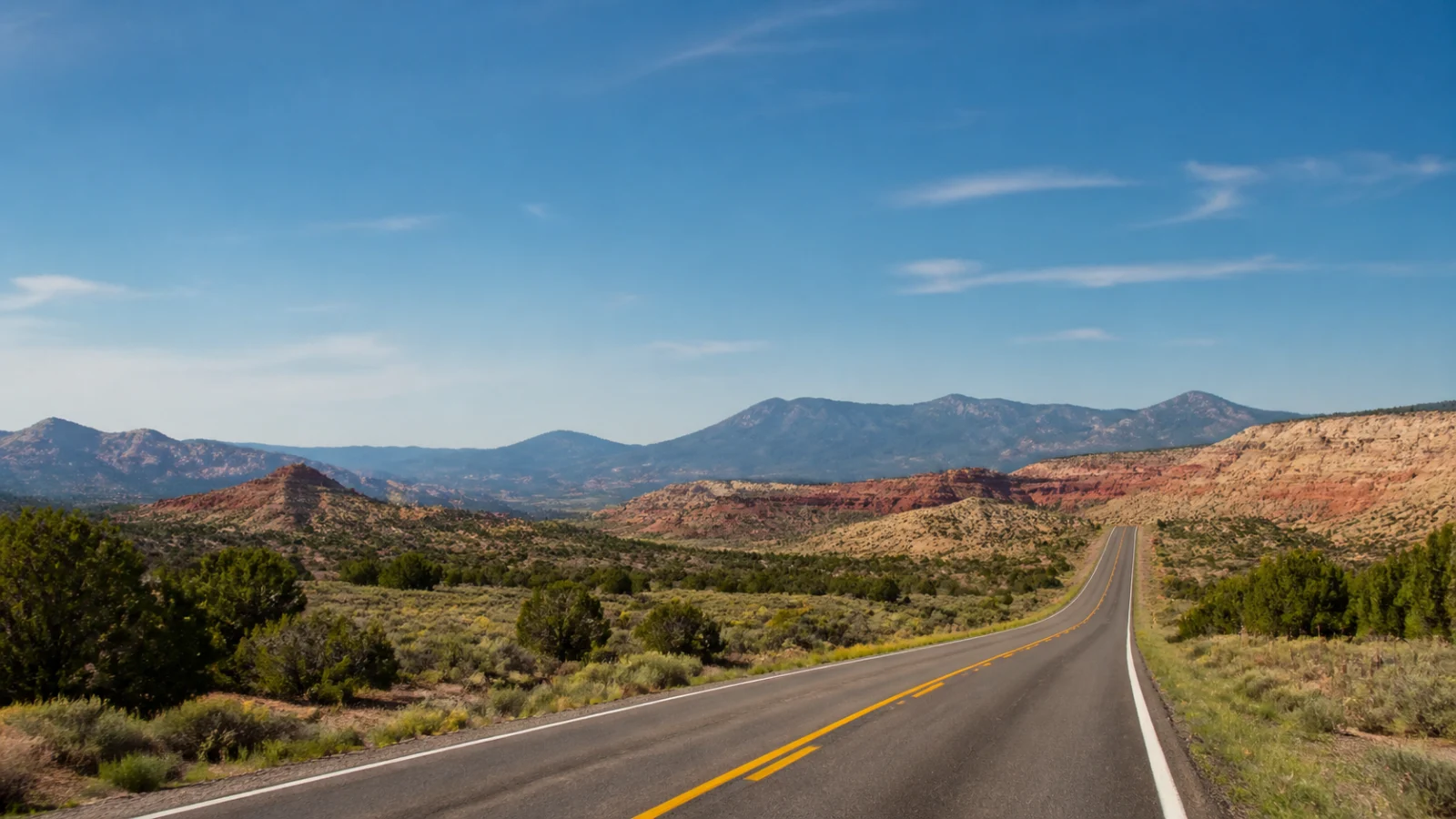 Breite Straße durch rote Felsen und Berge im Westen der USA bei klarem Sommerwetter