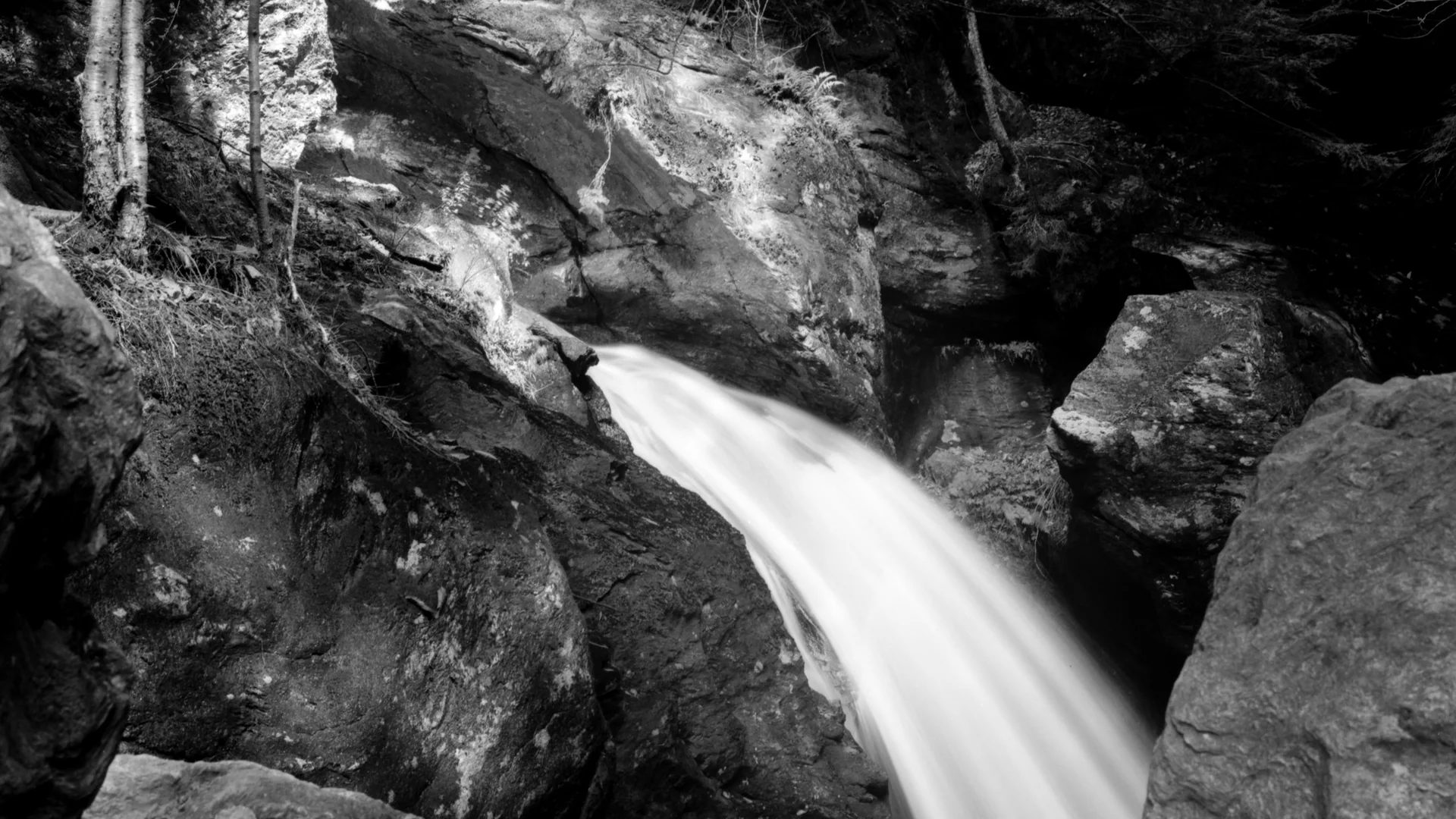Schwarzweißaufnahme eines Wasserfalls zwischen Felsen im Smugglers’ Notch State Park