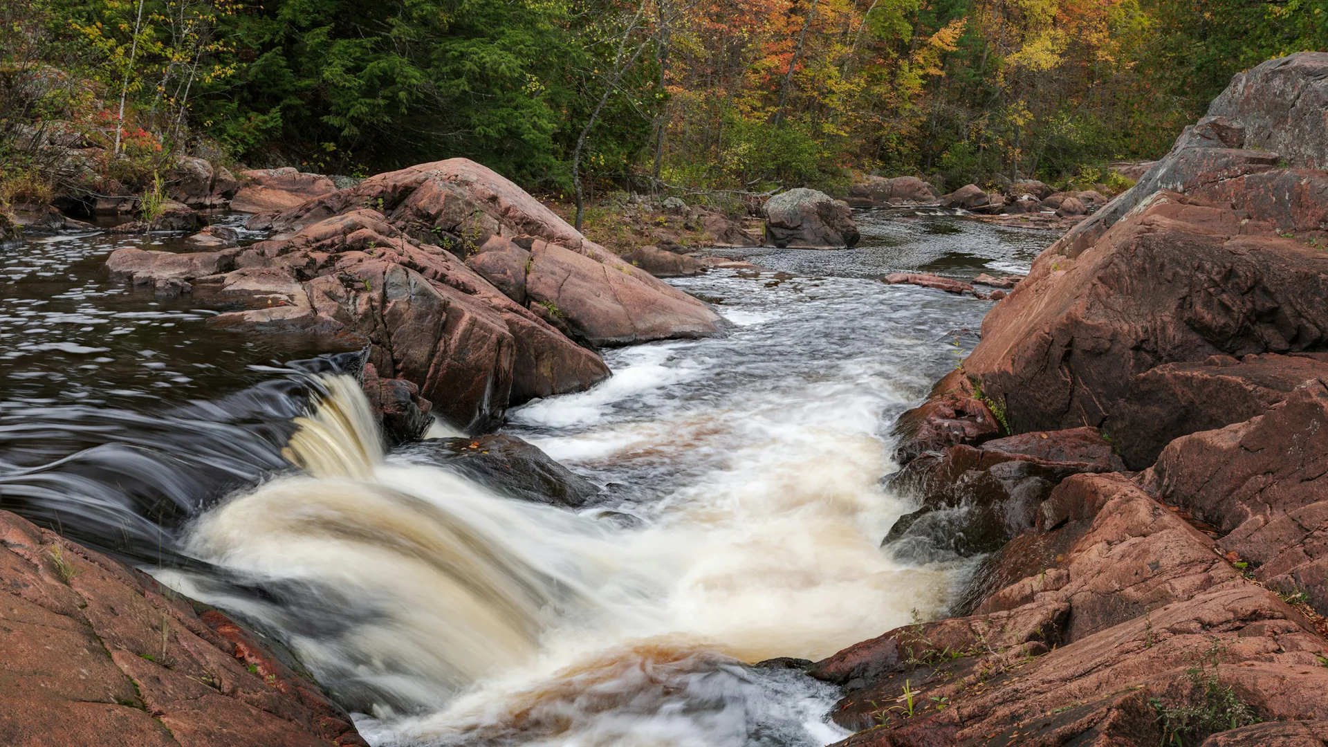 Stromschnellen fließen über rötliche Felsen bei Red Granite Falls im Copper Falls State Park