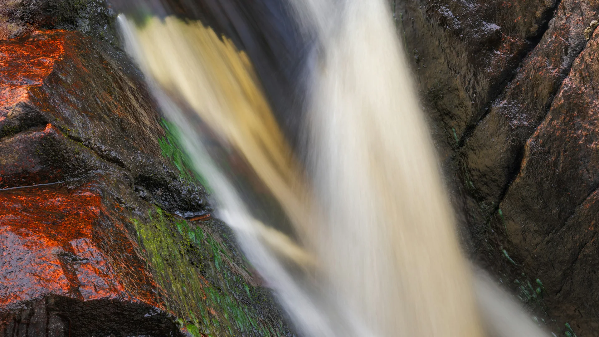 Nahaufnahme eines Wasserfalls zwischen dunklen und rötlichen Felsen im Copper Falls State Park