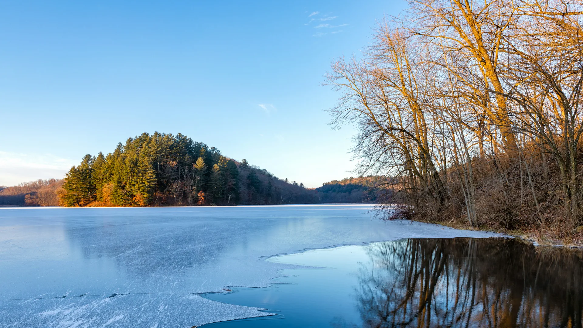 Teilweise gefrorener See und bewaldete Hügel im Governor Dodge State Park