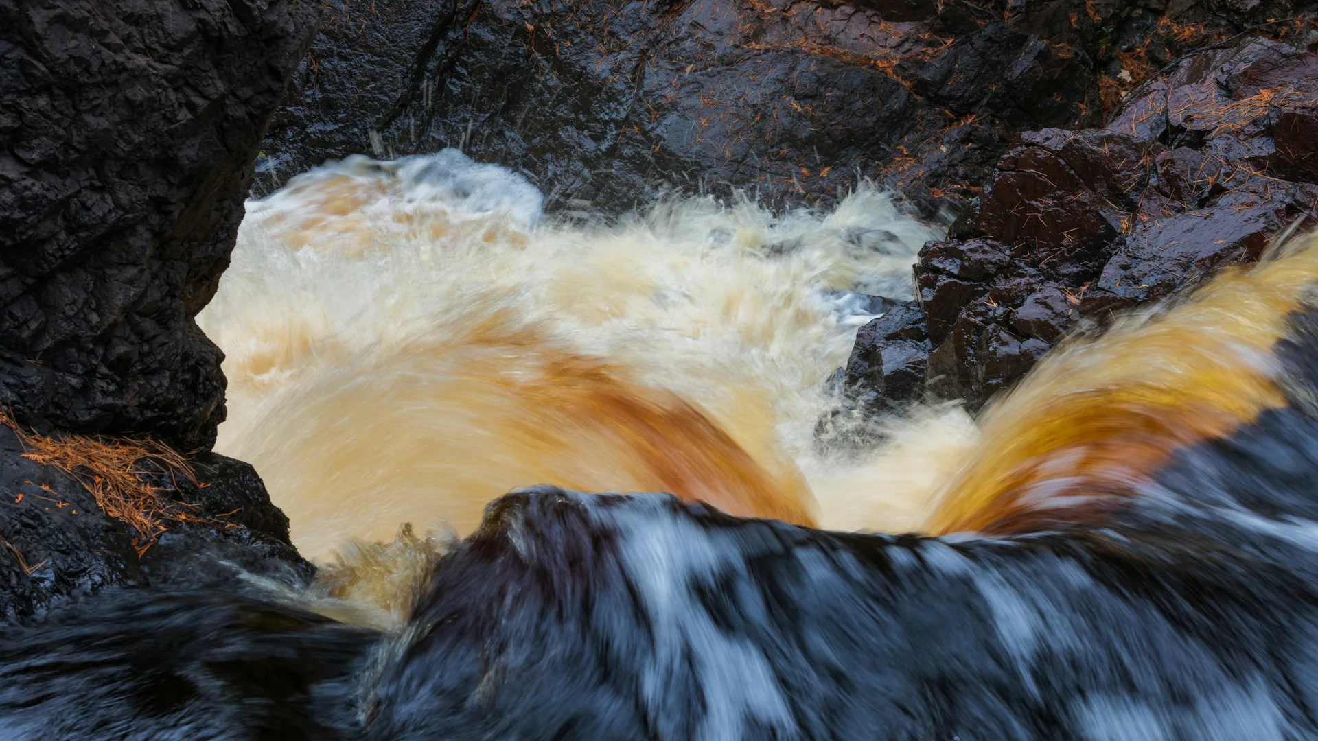 Braunes Flusswasser rauscht über dunkle Felsen im Pattison State Park
