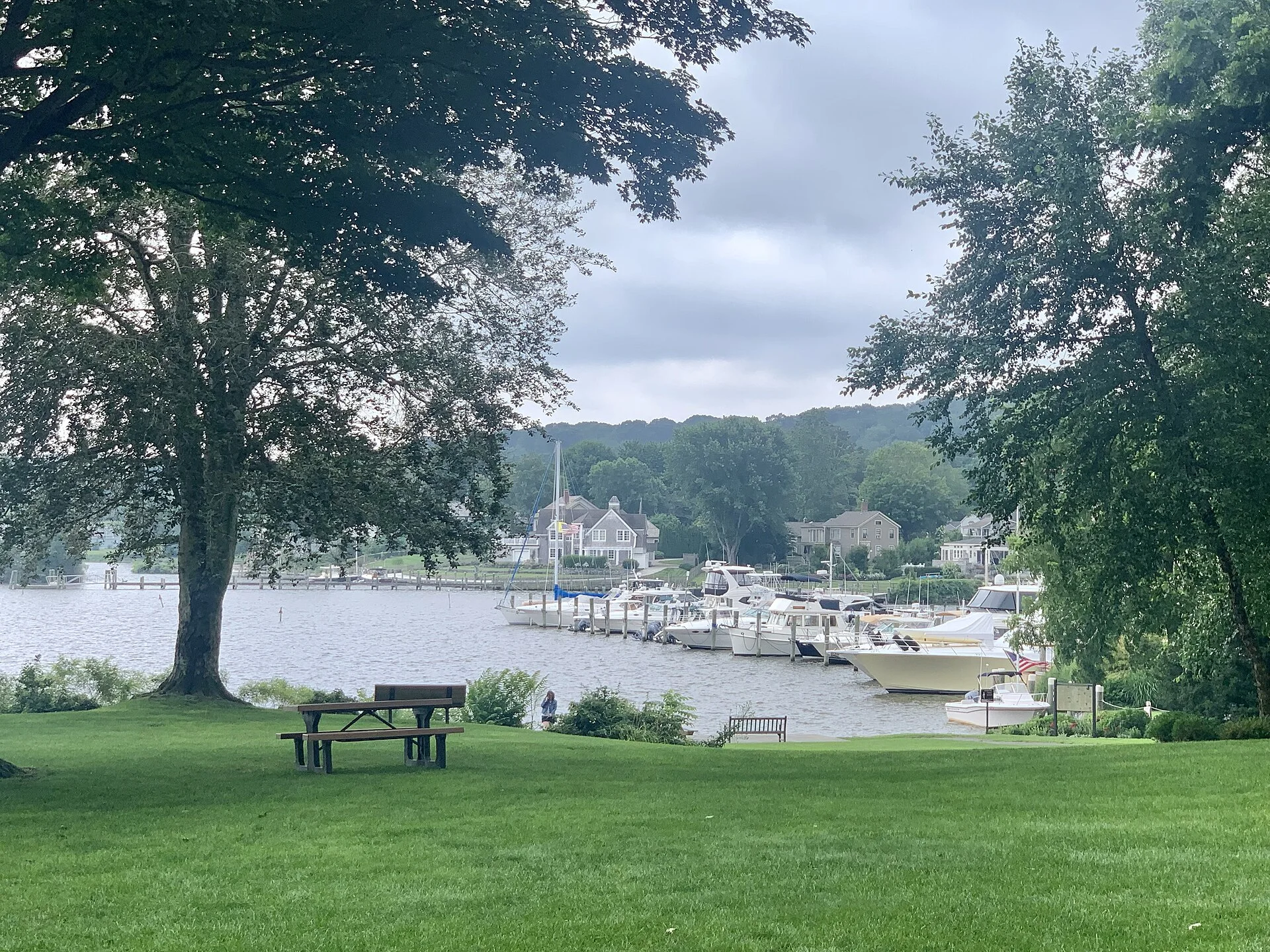 This image displays the waterfront of Essex Park in the foreground, located in Essex, Connecticut. The harbor is visible in the background.