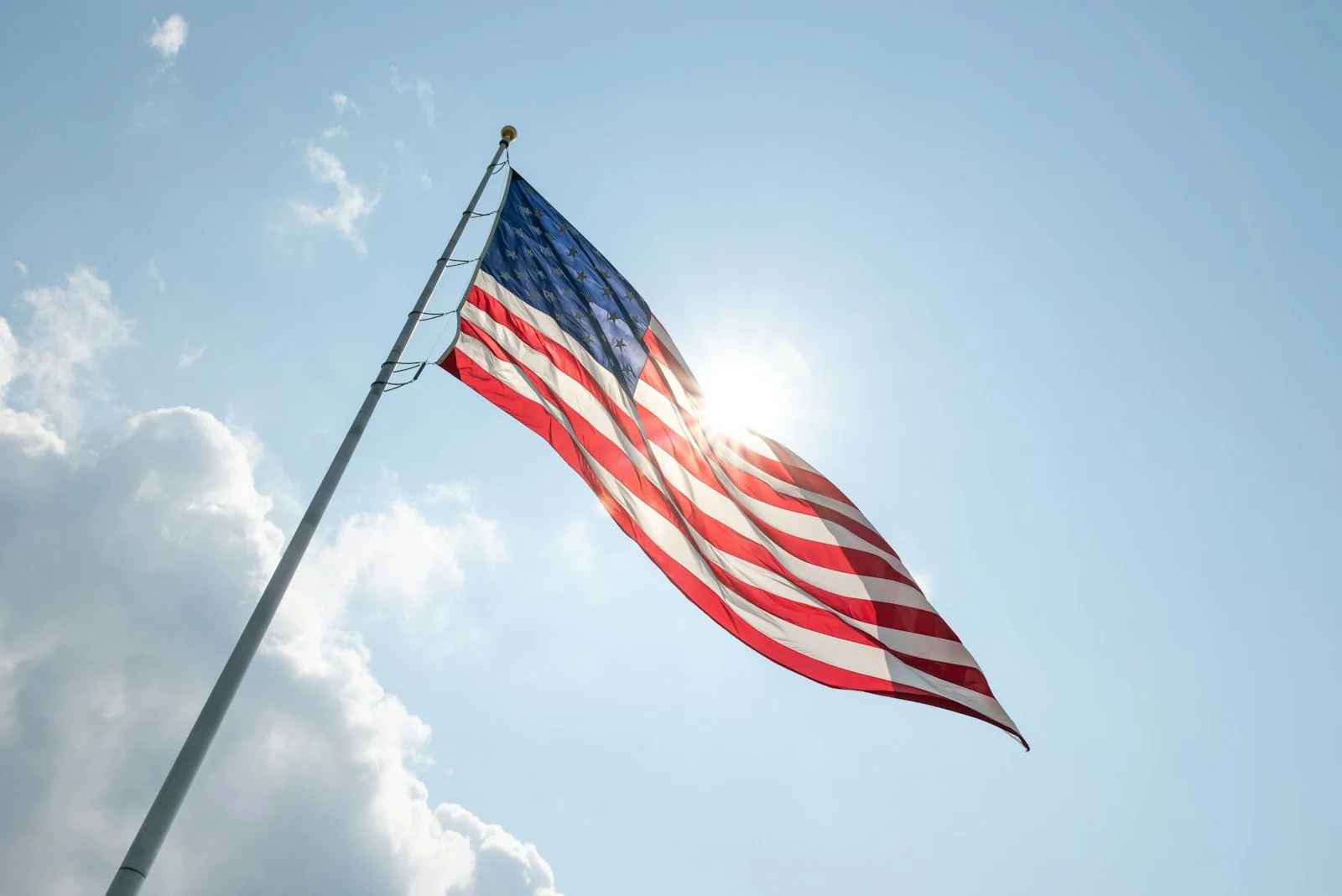 American flag waving against a bright blue sky with sun.