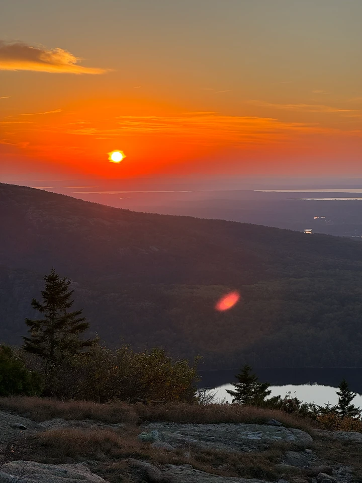 Orange Abendsonne über bewaldeten Hügeln und Wasserflächen vom Cadillac Mountain