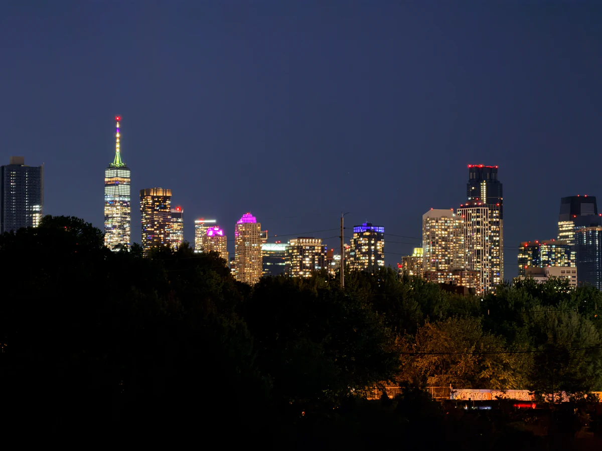 Beleuchtetes One World Trade Center hinter Gebäuden von Jersey City bei Nacht