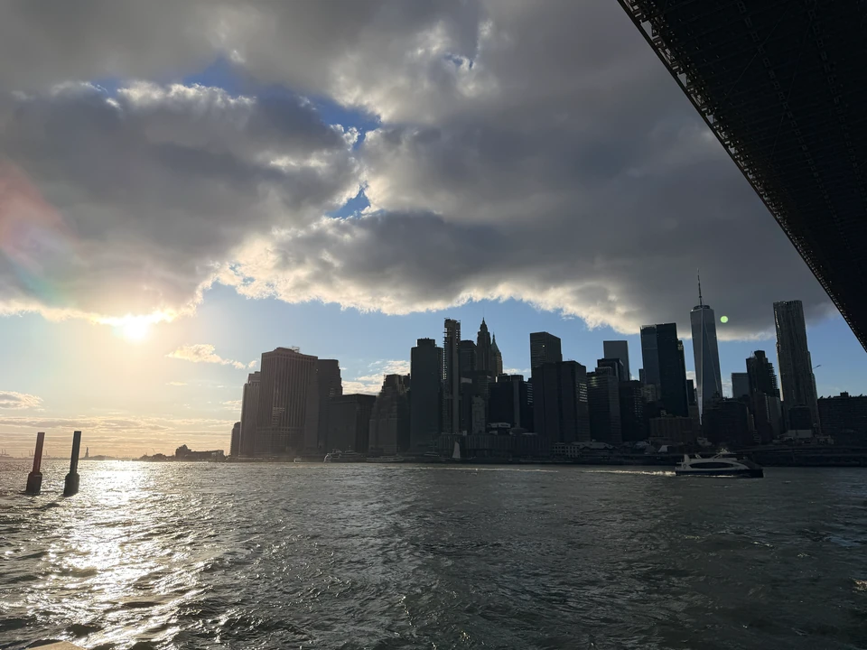 Tief stehende Sonne und Manhattan-Silhouette unter der Brooklyn Bridge
