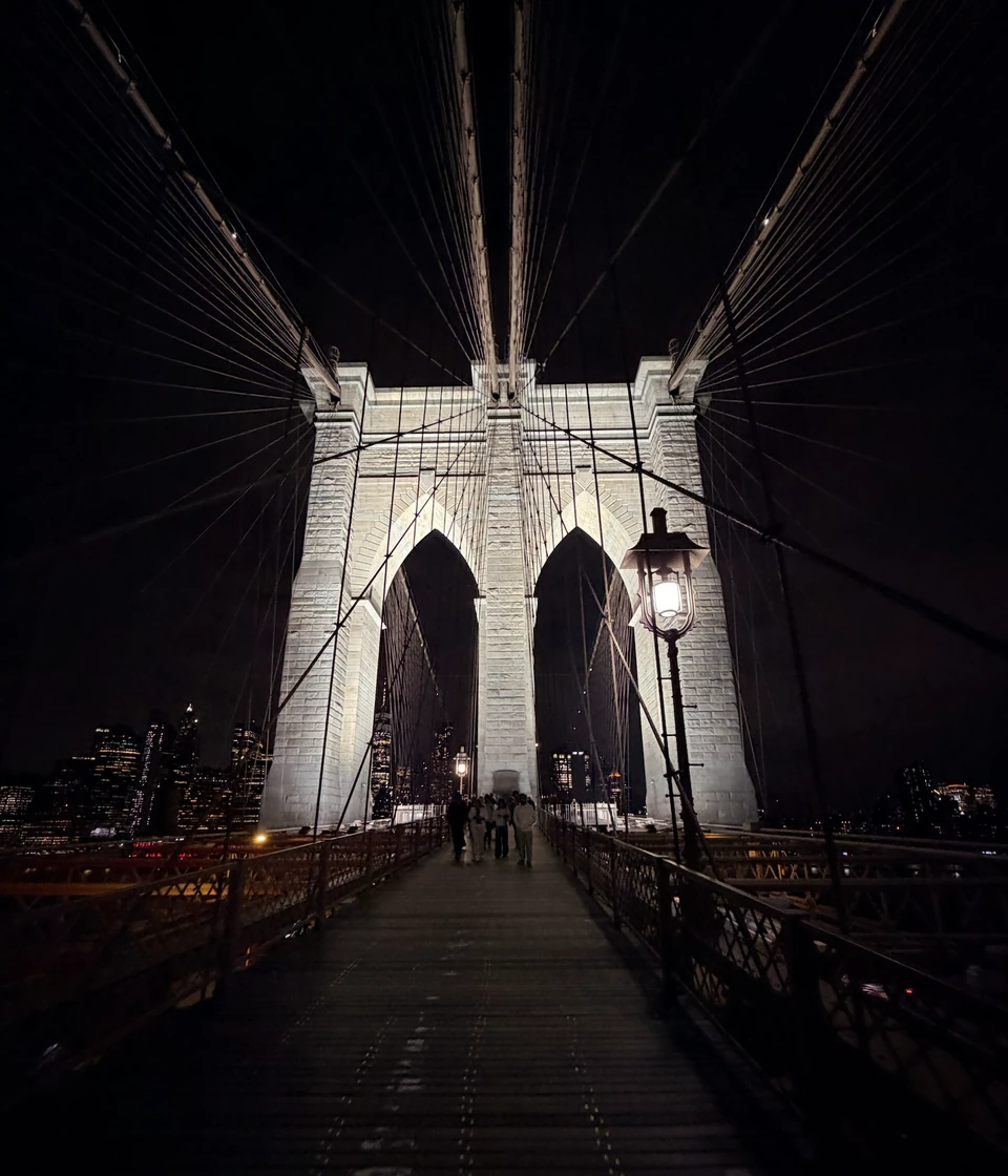 Beleuchteter Steinpylon und Tragseile über dem Fußweg der Brooklyn Bridge bei Nacht