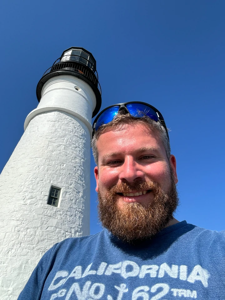 Tobias vor dem weißen Turm des Portland Head Light unter blauem Himmel